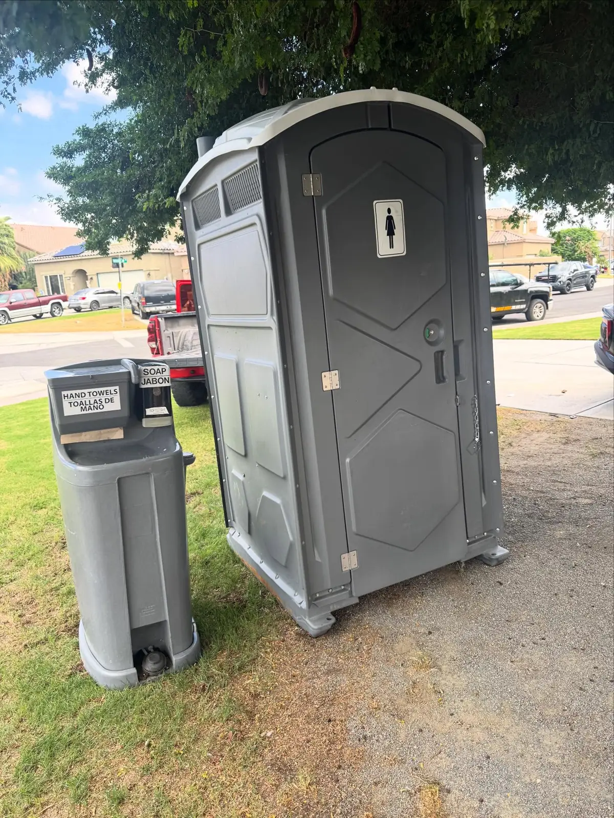 Gray PJN3 porta potty beside a Bravo hand wash station on a lawn, the level placement an accessible unit needs